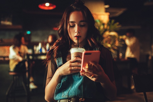 young lady on phone drinking iced coffee in moody coffee shop